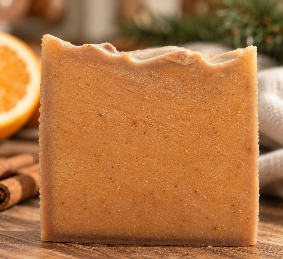 A rectangular Bare Daily Citrus and Clove Gingerbread bar of handmade soap with a rustic, unevenly broken top edge, standing upright on a wooden surface. The soap has a warm, golden-brown color with tiny dark specks.