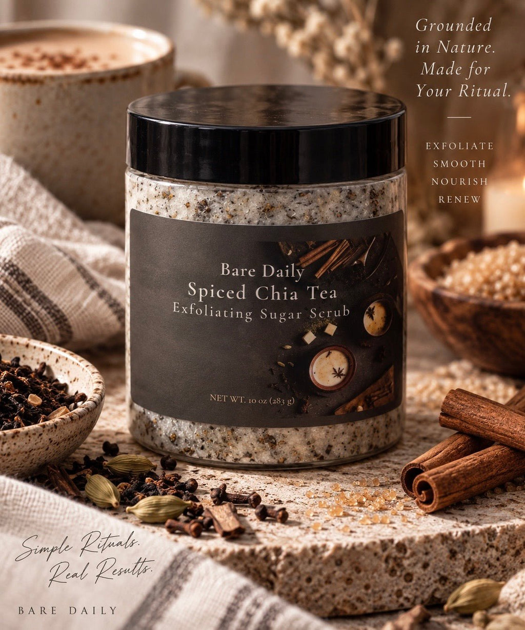 A jar of Bare Daily Spiced Chia Tea Exfoliating Sugar Scrub sits on a stone surface surrounded by cinnamon sticks, cardamom pods, and bowls of ingredients. The product has a black lid and a dark charcoal label with warm beige and brown tones.