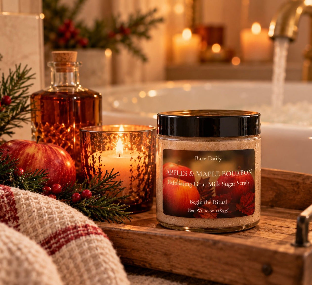 Bare Daily Apples and Maple Bourbon Exfoliating Goat Milk Sugar Scrub 10 oz jar on a wooden bath tray next to a lit candle, red apples, and a running bathtub.