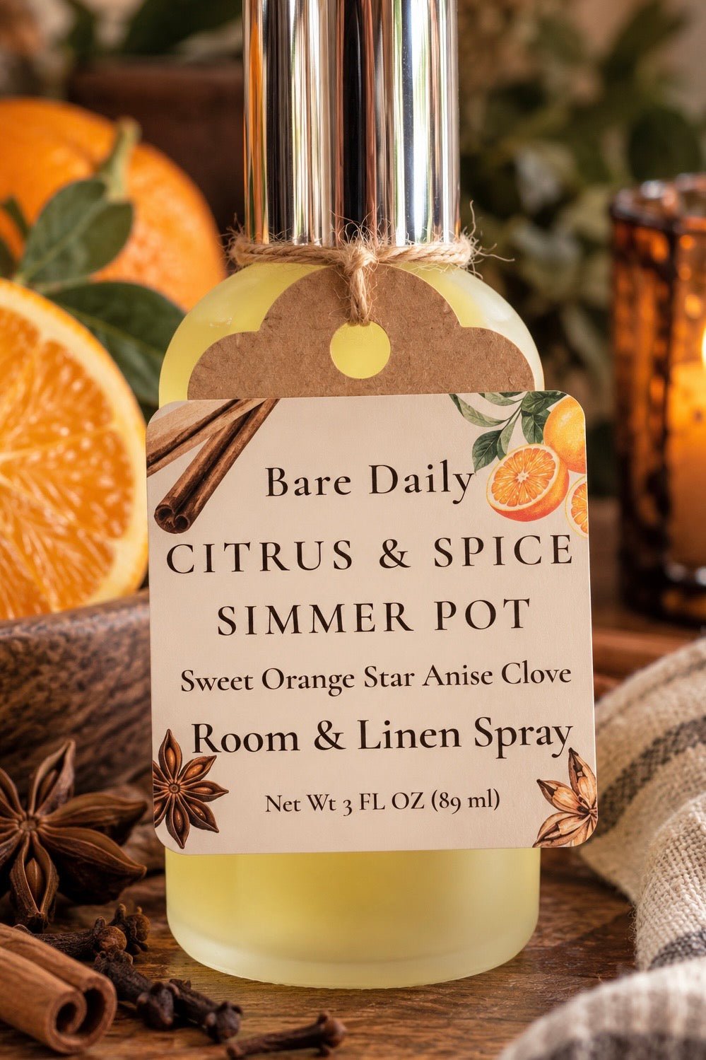 A bottle of Bare Daily Citrus & Spice Simmer Pot room and linen spray, styled with citrus slices, cinnamon sticks, star anise, and a warm candle in the background.