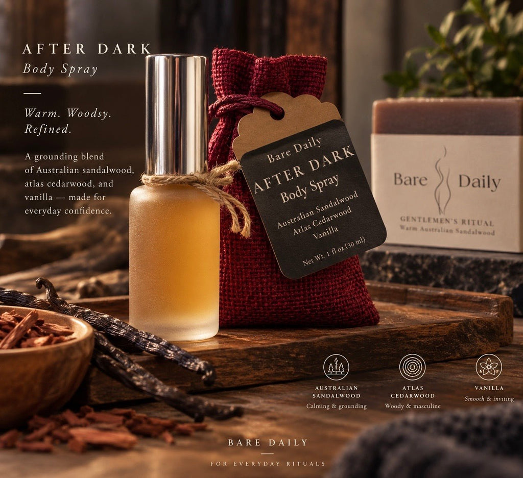 A bottle of Bare Daily After Dark Body Spray stands on a wooden surface beside a red fabric drawstring pouch with a black product tag. The scene includes vanilla pods, a soap bar, and branded packaging in a styled, warm rustic setting with text describing the scent as warm, woody, and refined.