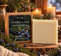 Bare Daily Juniper and Pine Artisan Goat Milk Soap bar next to its kraft packaging styled with evergreen branches.