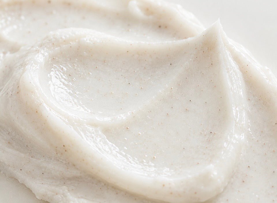 A close-up of a thick, creamy off-white cosmetic or food product with tiny dark specks, swirled on a light background.