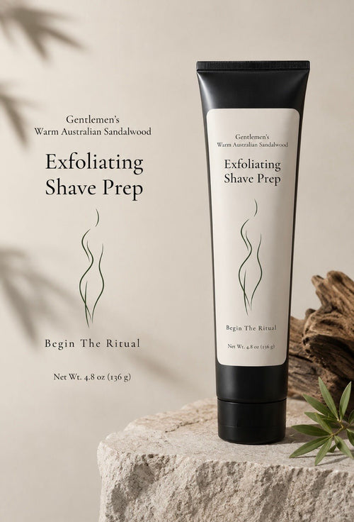  (Exfoliating Shave Prep tube on stone pedestal, driftwood, eucalyptus) Bare Daily Gentlemen's Warm Australian Sandalwood Exfoliating Shave Prep 4.8 oz tube standing on a stone pedestal with driftwood and eucalyptus leaves on a warm beige background — "Begin The Ritual"